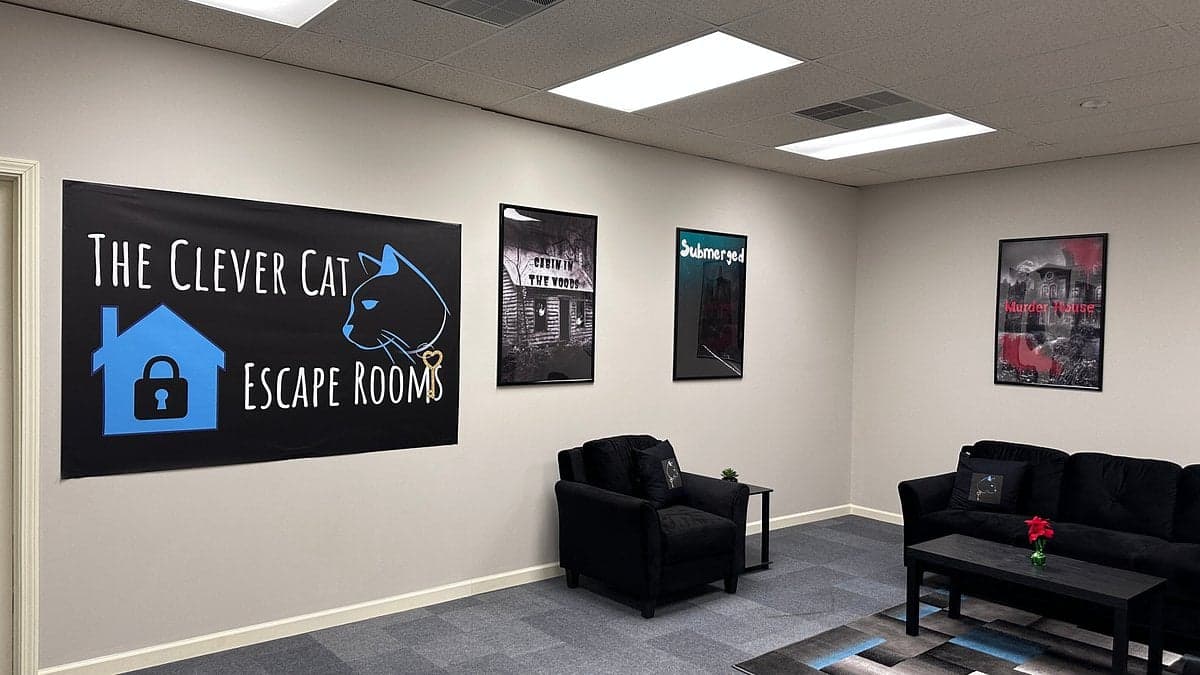The Clever Cat Escape Rooms banner above a seating area with posters. Escape room waiting area.