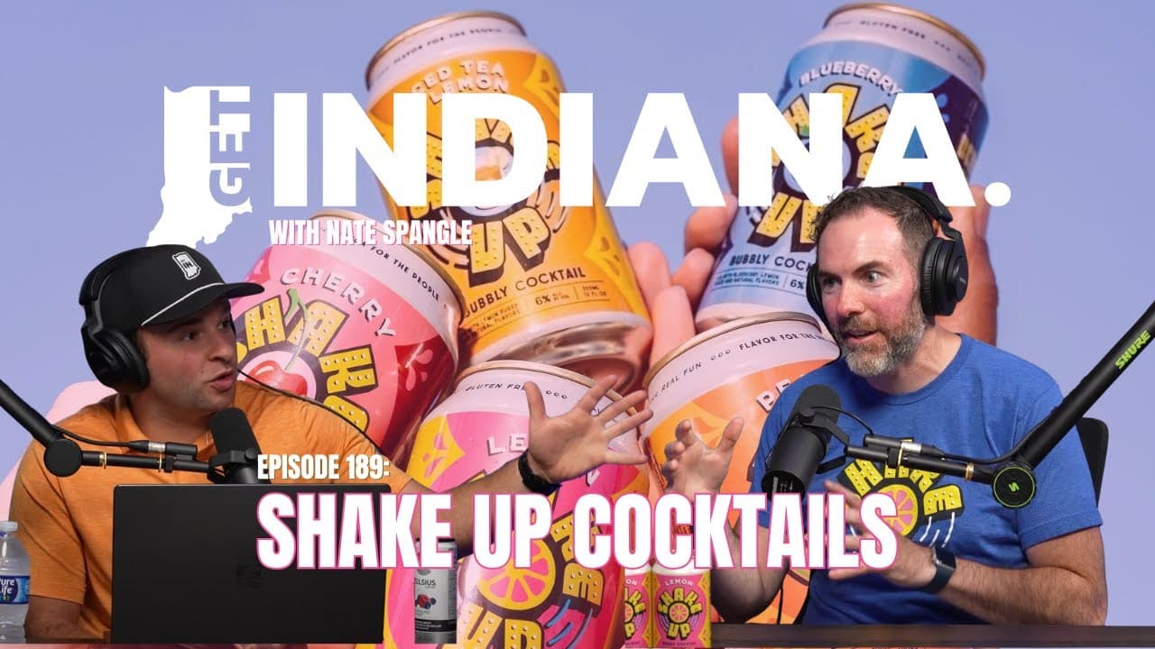 Two men discuss Indiana's cocktail startup, surrounded by colorful canned drinks on a podcast set.